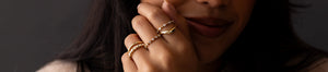 Woman wearing four 14k gold rings on her hand. A Diamond Distance Band, Petite Diamond Distance Band, and Sapphire Sapling Ring