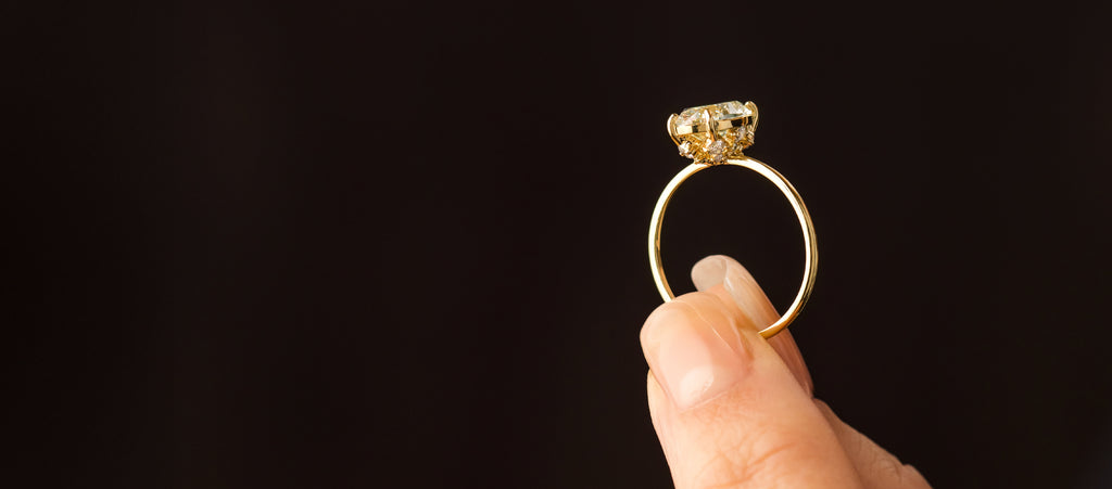 Photo shows a model holding up the Melanie Casey Wreathed Ring with a champagne diamond, showing off it's side profile.