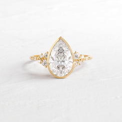 Snowdrift Ring in Pear Cut Engagement Ring in Yellow Gold by Melanie Casey shown on a textured white background