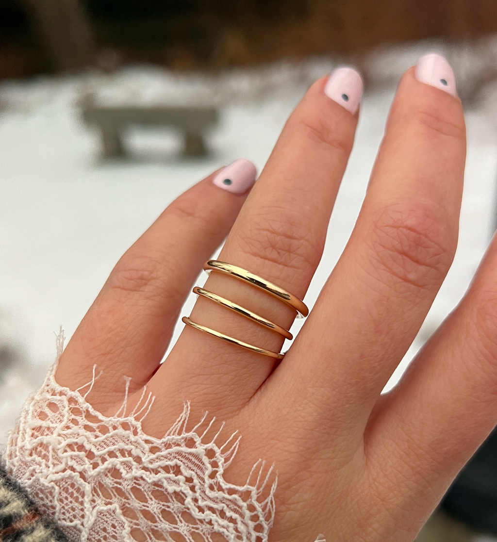 This photo showcases a model's hand with three different pairing bands on her ring finger, spaced apart so as to show each band's different width against a snowy, out-of-focus background.
