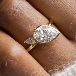 This photo showcase a model wearing the Upcast Engagement Ring in Pear cut with a 2mm width band.