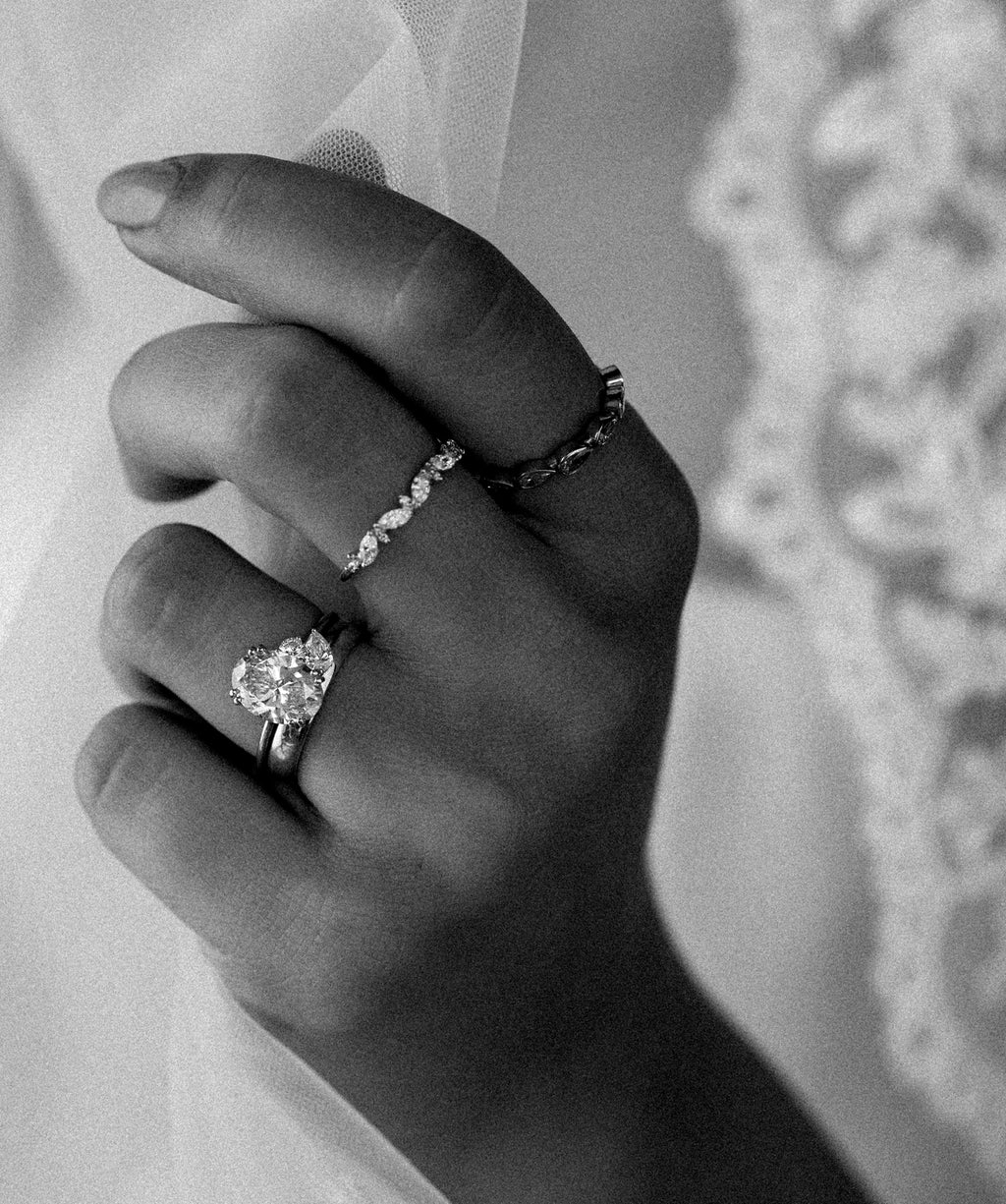 Photo showcases a woman's hand with a variety of Melanie Casey rings holding a lace wedding veil.