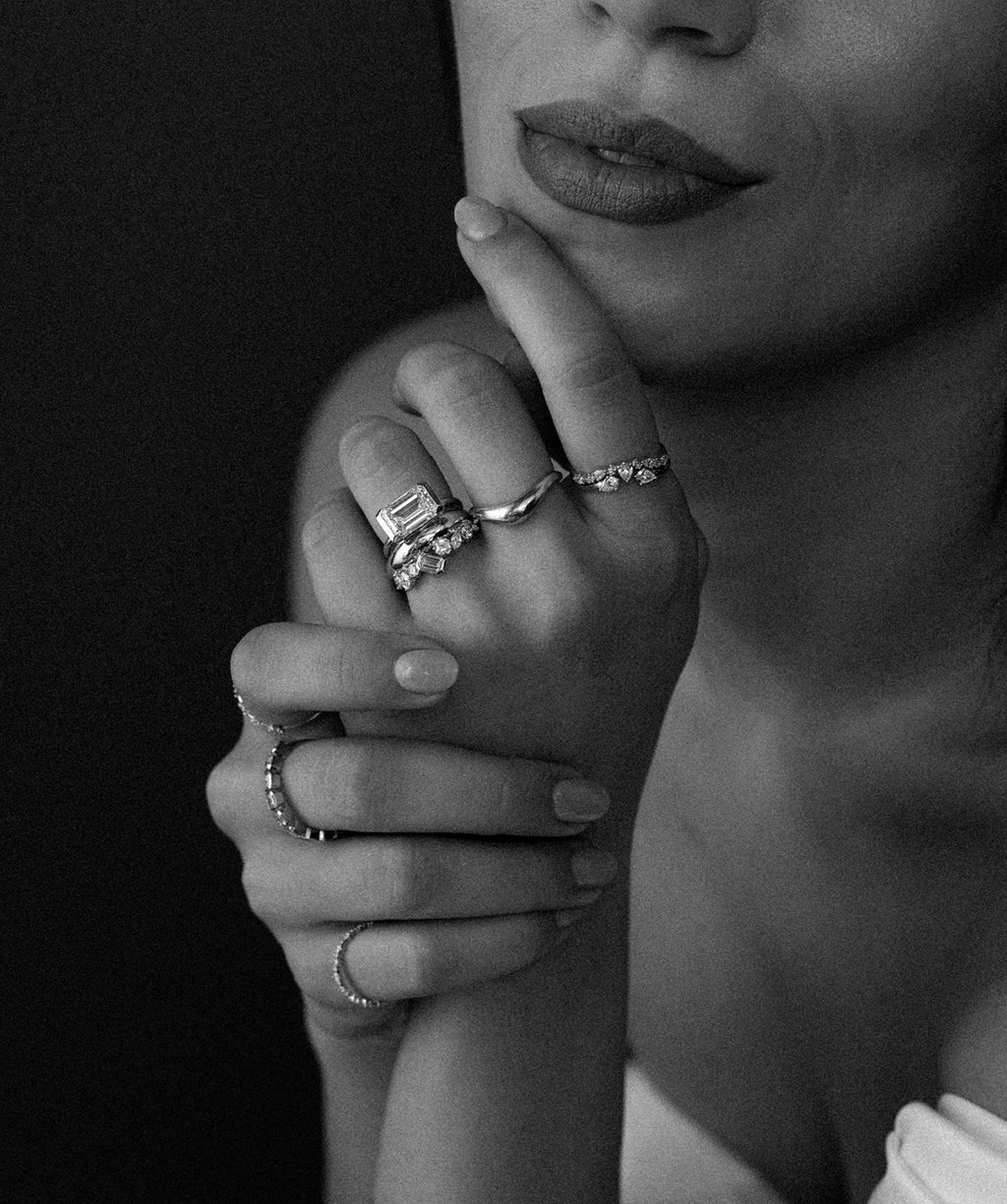 This black and white photo showcases a model wearing a mix of Melanie Casey rings who is resting her hand on her chin with a slight smile on her face.