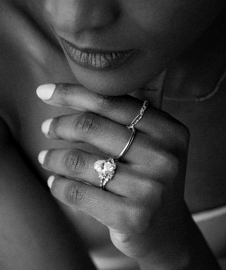 This black and white photo showcases a woman wearing an assortment of Melanie Casey rings, holding her hand up and touching her chin with a slight smile on her face.