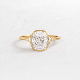 Evenfall Cushion Cut Engagement Ring in Yellow Gold by Melanie Casey shown on a textured white background