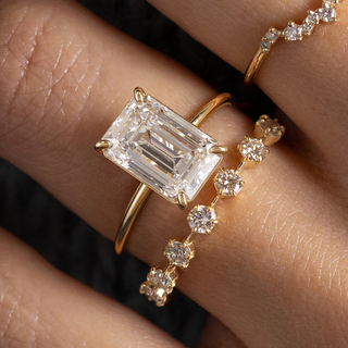 This photo showcase a model wearing a dainty Whisper Engagement Ring in Emerald cut with a 1.2mm width band