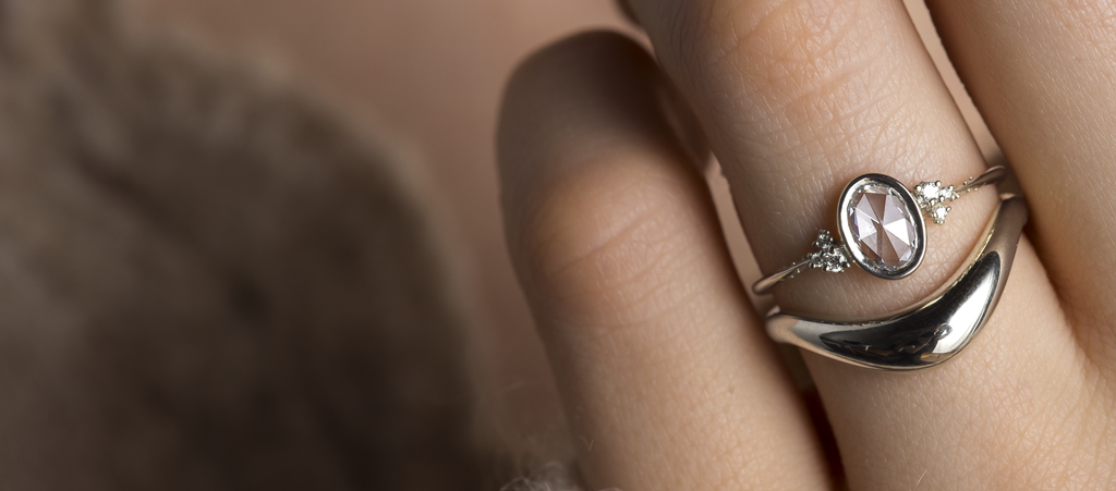 Photo features someone wearing an oval rose cut bezel set Melanie Casey engagement ring.