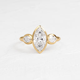Moonrise Ring in Marquise Cut Engagement Ring in Yellow Gold by Melanie Casey shown on a textured white background