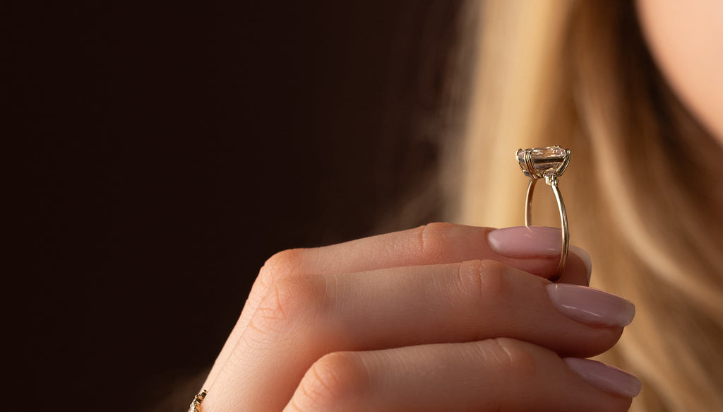 This photo features a model holding up the Melanie Casey Pictorial Ring, showcasing it's 3/4 profile view and highlighting it as a dainty engagement ring.
