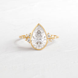 Snowdrift Ring in Pear Cut Engagement Ring in Yellow Gold by Melanie Casey shown on a textured white background