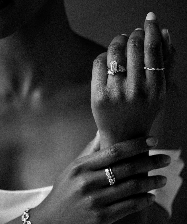 This black and white photo features a model wearing a bridal gown and an assortment of Melanie Casey jewelry, with one hand resting on her wrist and the other held up to show off the wedding set.