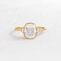 Evenfall Cushion Cut Engagement Ring in Yellow Gold by Melanie Casey shown on a textured white background