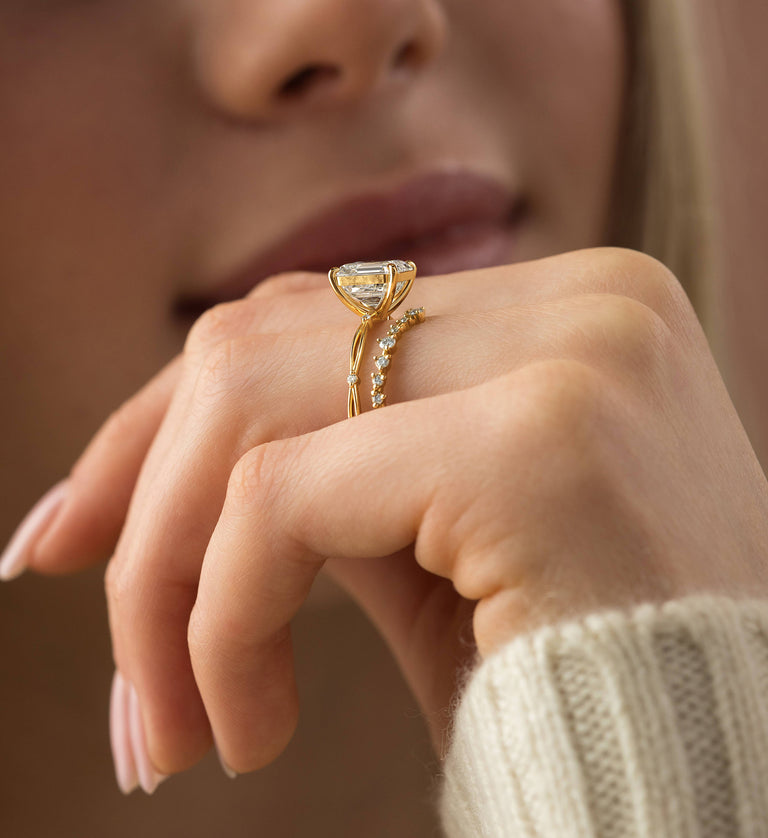 This photo features a model wearing the Melanie Casey 14k Yellow Gold Hillside Ring in Asscher Cut paired with the Many Moons Band on her ring finger. She is holding her hand up in front of her face so that the side profile of both rings are showcased.