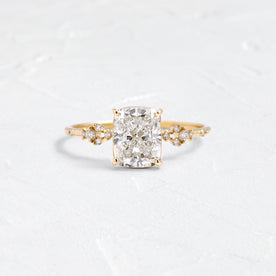 Myriad Cushion Cut Engagement Ring in Yellow Gold by Melanie Casey shown on a textured white background