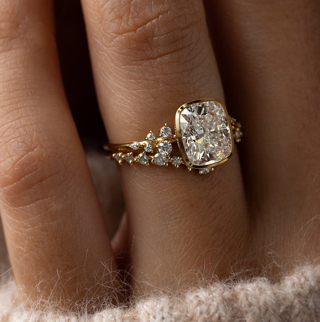 Model wearing the Melanie Casey Snowdrift Bezel Set Ring with a Cushion Cut center stone, shown from a three quarter side profile view.