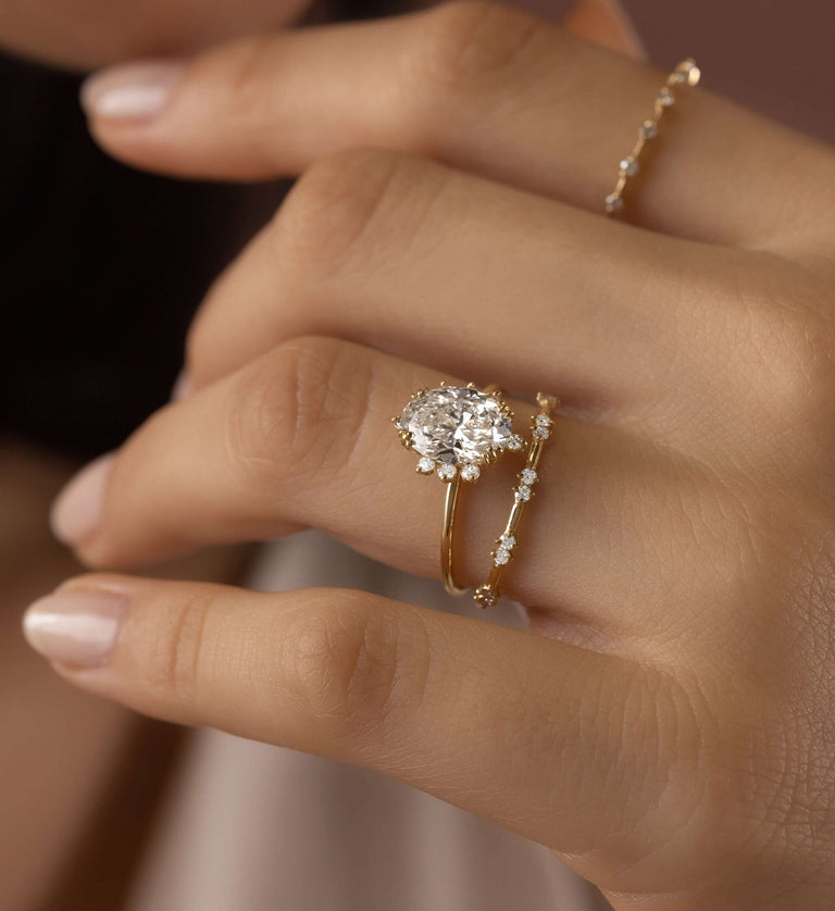 This photo features a model wearing the Melanie Casey 14k Yellow Gold Threaded Engagement Ring with Halo in Oval Cut on her ring finger. She is holding her hand up in so that the 3/4 profile view of the ring is showcased.