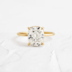 Whisper Cushion Cut Ring Engagement Ring in Yellow Gold by Melanie Casey shown on a textured white background