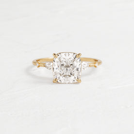 Windlass Cushion Cut Ring Engagement Ring in Yellow Gold by Melanie Casey shown on a textured white background