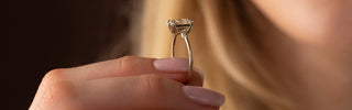 This photo features a model holding up the Melanie Casey Pictorial Ring, showcasing it's 3/4 profile view and highlighting it as a dainty engagement ring.